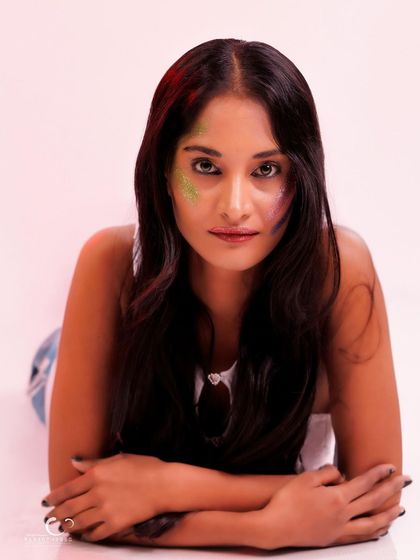 A direct and engaging portrait against a clean white background. The focus is on her expression and the creative makeup.