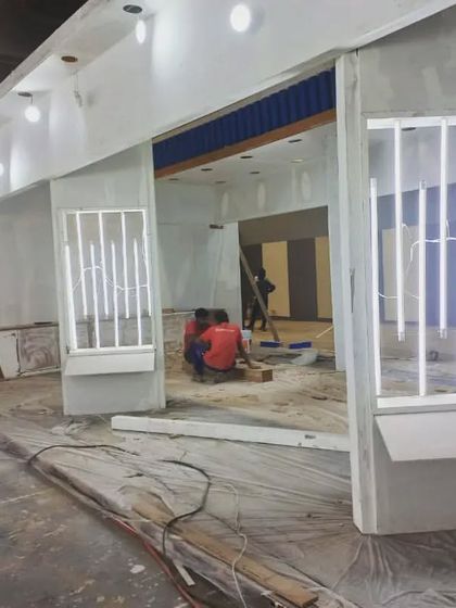 A view of a booth under construction, with workers installing lighting fixtures and wall panels.