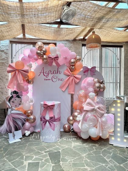 The complete setup for the bow-themed first birthday party for 'Ayrah', designed for a restaurant or cafe venue.