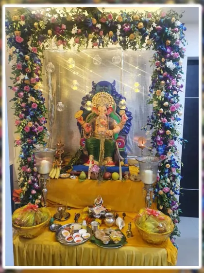 This elegant Ganpati setup features a floral arch with a mix of blue, pink, and white flowers. The subtle lighting and silver backdrop add a touch of sparkle, enhancing the beauty of the idol and the offerings.