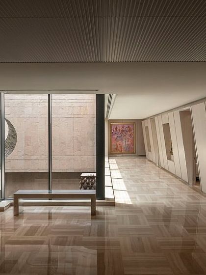 The second-floor corridor of 'The Layered Office' is designed as a gallery-like space. It features views into the central courtyard, polished marble floors, and wall niches for displaying art, creating a refined circulation path.