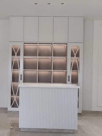 A full view of the custom bar unit for Aura Designgram, showing the combination of closed overhead storage, illuminated display cubbies, and a fluted bar counter. This piece was designed for both grand entertaining and practical storage.