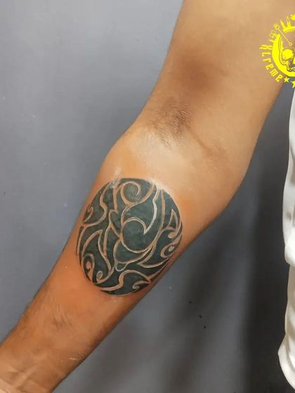 An abstract circular tattoo on the elbow. This design uses negative space to create a flowing, organic pattern that is both modern and unique.