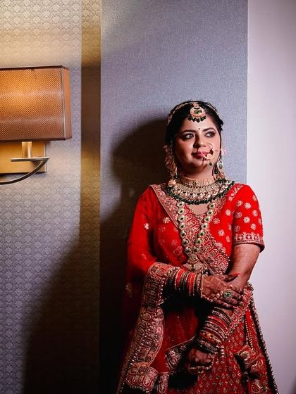 A full-length portrait of the bride in her stunning red lehenga. The dramatic side lighting creates a sophisticated and elegant look, highlighting the rich texture of her outfit.