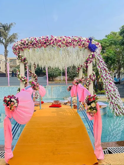 For a poolside wedding, I designed this unique mandap featuring a floral peacock. The structure is adorned with pink and white flowers, creating a stunning visual that appears to float over the water.