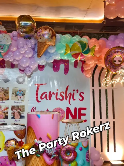 The main backdrop for the Candyland first birthday, featuring a "Sweet One" sign, a photo collage, and a balloon arch that looks like melting ice cream.