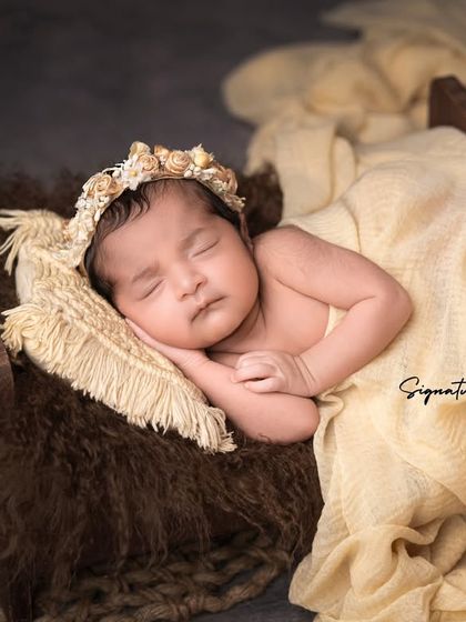 A sleeping newborn girl in a rustic wooden bed, adorned with a delicate floral headband.