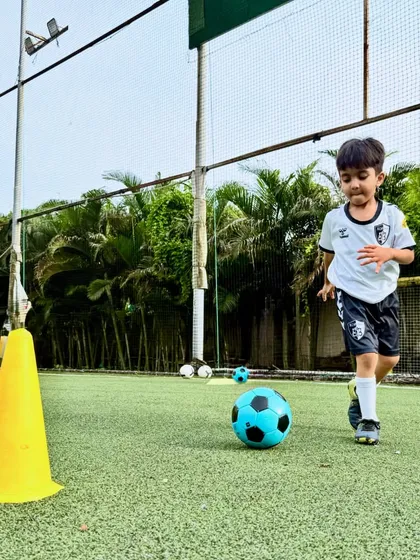 A young player from our U6 batch focuses intently as he dribbles past a cone, learning the basics of ball movement on our professional turf.