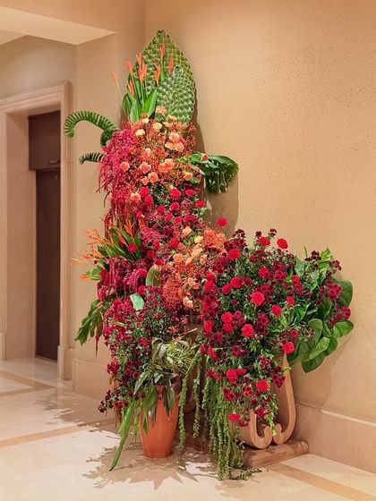 A magnificent, cascading floral sculpture in shades of red and orange. The asymmetrical form and mix of tropical flowers and classic roses create a piece that is both wild and sophisticated.