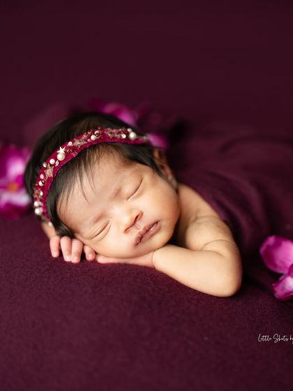 A beautiful side profile of a sleeping baby, highlighting their delicate features against a rich plum background.