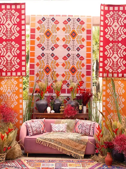 The main seating for our African tribal-themed event. A pink sofa is set against a backdrop of bold, geometric-patterned fabric panels, framed by dried grasses and colorful flowers.