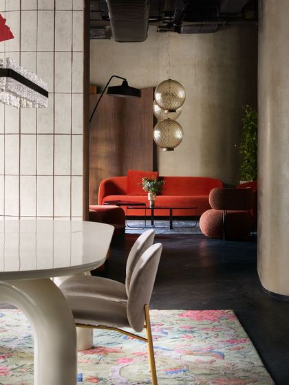 A glimpse from a dining area into a living room setup with a vibrant red sofa. The design uses sightlines and layered spaces to encourage exploration and discovery within the store.