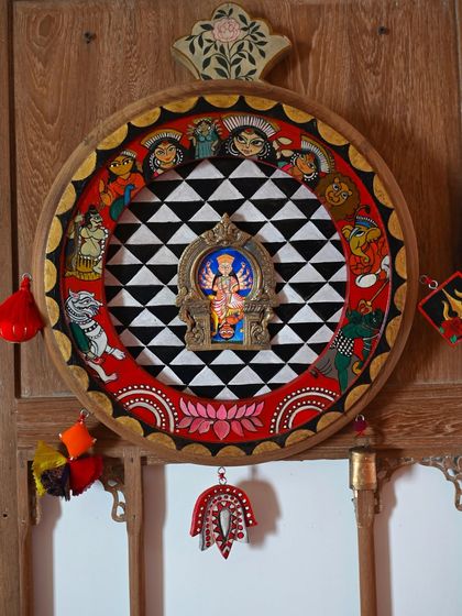 The Durga frame displayed against a wooden jharokha, highlighting its traditional yet contemporary appeal. The piece is adorned with handmade tassels and bells, adding to its protective, dreamcatcher-like quality.
