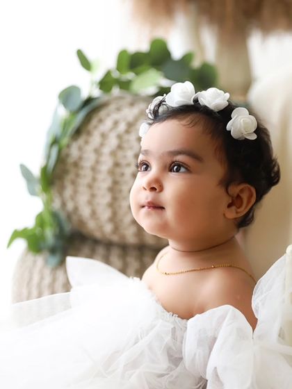 A profile shot of a baby girl in a white dress, looking thoughtfully to the side in a beautifully lit portrait.