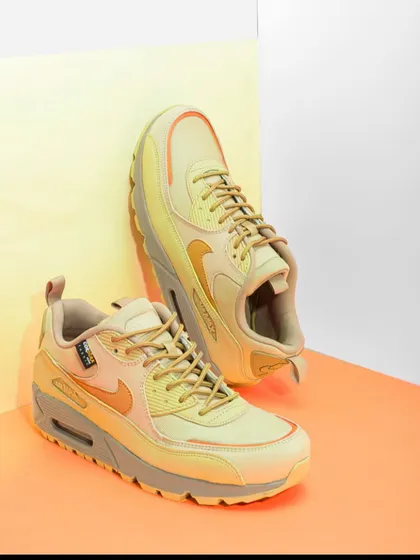 A pair of pastel yellow Nike Air Max sneakers styled with simple, overlapping colored cards. This adds depth and context to the shot while maintaining a clean, minimalist aesthetic.