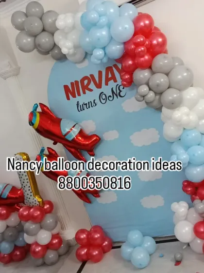 An adventurous airplane theme for a first birthday party. This setup includes a sky-themed backdrop, red airplane foil balloons, and a balloon arch in red, grey, and light blue.