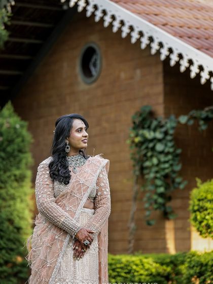 A candid and elegant portrait of a bride at her reception, looking off to the side in a beautifully embroidered lehenga, captured in a lovely garden setting.