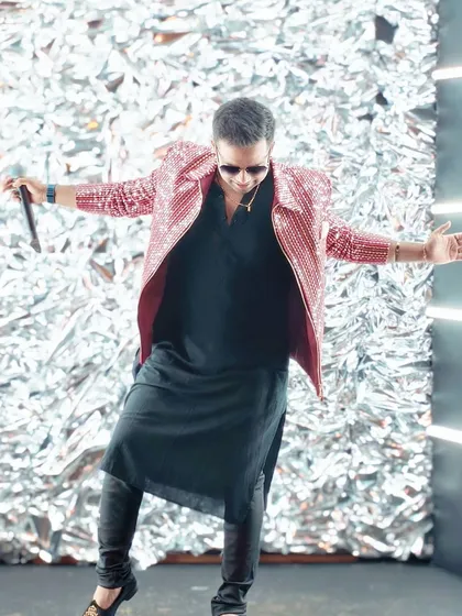 A full-body shot showcasing my dynamic stage presence. The combination of a long black kurta and a shiny jacket creates a perfect fusion look for a modern sangeet.
