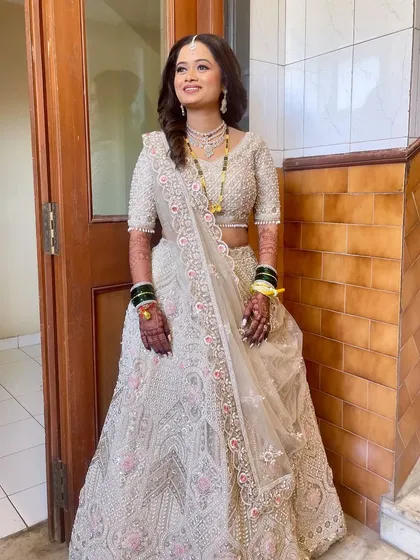 A full-length shot of a reception bride in a stunning ivory lehenga. The hairstyle is soft and romantic with side-swept curls.