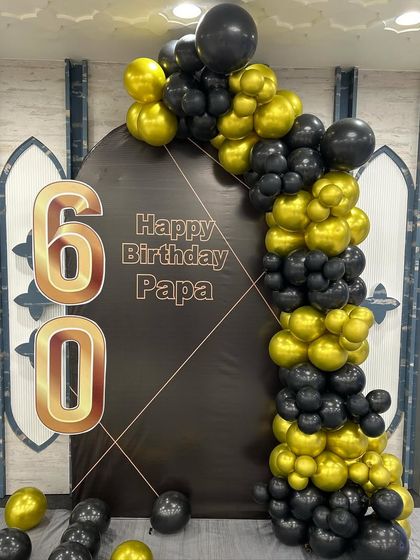 A classic and stylish 60th birthday decoration for a father. This simple setup features a black arched backdrop with 'Happy Birthday Papa' and a sophisticated black and gold balloon garland.