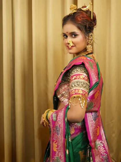 A side profile against a simple backdrop, emphasizing the rich colors of her saree and the intricacy of her hairstyle.