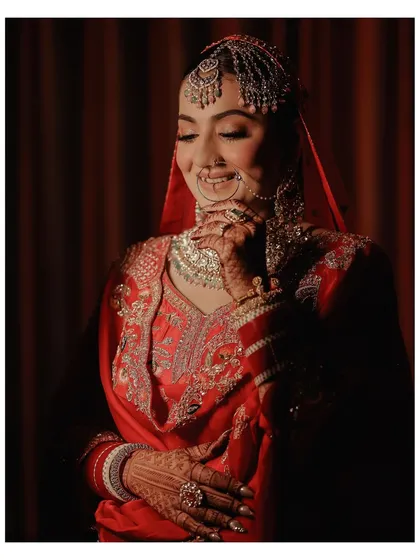 A close-up portrait of the bride, her face softly lit. This shot captures her gentle smile and the intricate details of her nath, jewelry, and mehndi.