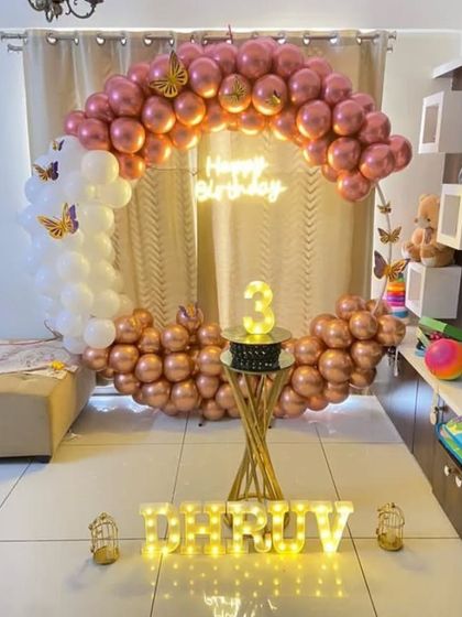 An elegant butterfly theme with a rose gold and white balloon arch. This home setup features a 'Happy Birthday' neon sign and light-up letters, creating a chic and modern party look.