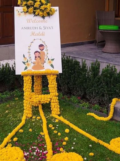 A personalized welcome sign for a Haldi ceremony, decorated with fresh marigold flowers to greet guests.