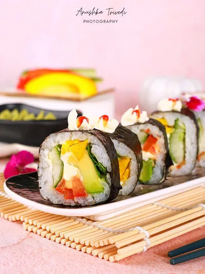 A line of the veggie sushi rolls, showing their colourful filling of avocado, cucumber, and bell peppers. The composition is clean and minimalist.