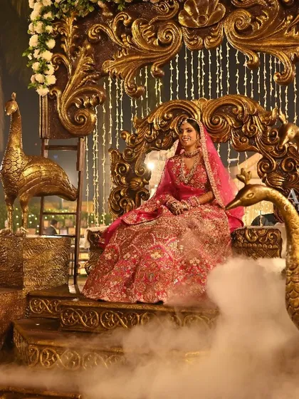 A close-up of the bride seated on her royal palanquin, adorned with golden peacock statues. The low-lying smoke adds a mystical effect to her regal and serene entrance.