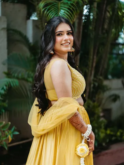 A side profile showing the soft waves and floral details in her hair. The makeup is dewy and light, perfect for a sunny outdoor event.