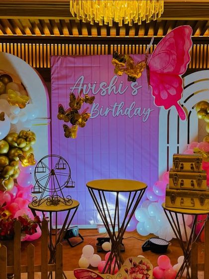 Another angle of 'Avishi's' butterfly-themed birthday, highlighting the gold and pink color scheme, decorative picket fence, and Ferris wheel prop.