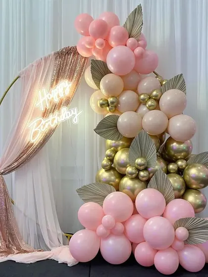 I love creating elegant and chic setups like this one. This beautiful photo corner features a gold ring draped with sequined and sheer fabric, a custom 'Happy Birthday' neon sign, and a stunning balloon cascade in pink, peach, and chrome gold.