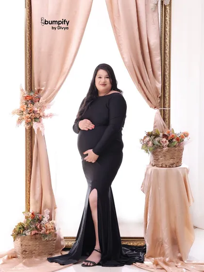 A confident solo portrait of the mom-to-be in a classic black gown. The soft pink drapes and floral arrangements add a touch of romance to the scene.