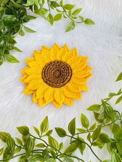 Another view of the large, double-layered crochet sunflower, surrounded by green leaves. It’s a beautiful piece that can be used to decorate bags or as a standalone flower.