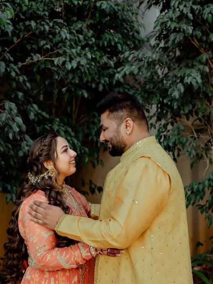 A candid couple moment from a Haldi function. The groom wears a simple yellow kurta with mirror work, designed to complement the bride's embellished outfit.