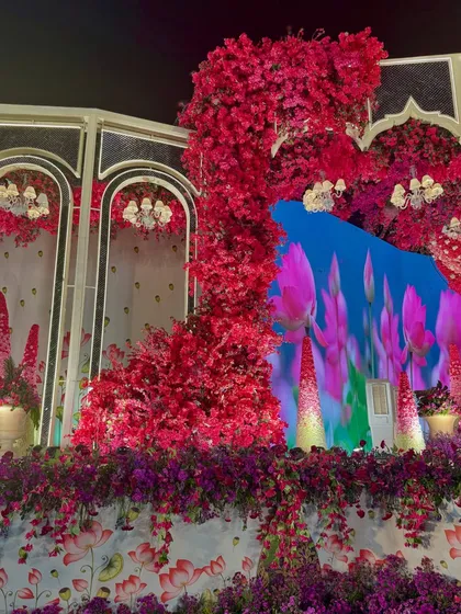 A side view of the stage, where a wall of red flowers is set against a digital backdrop of lotus flowers, blending physical and digital art.
