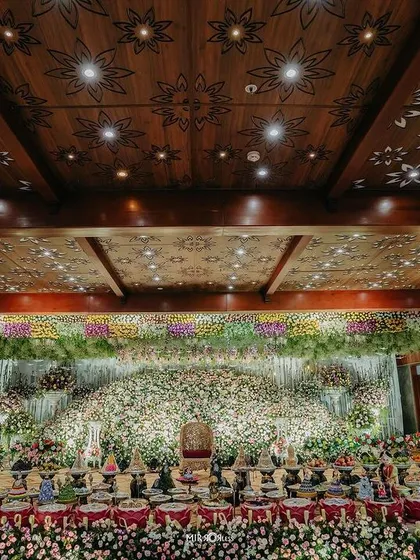 A wide shot of a grand floral stage, with a beautifully lit carved wood ceiling.