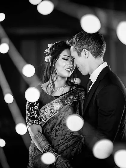 A romantic black and white portrait of a couple surrounded by bokeh lights. The soft focus and intimate embrace create a dreamy and timeless feel.