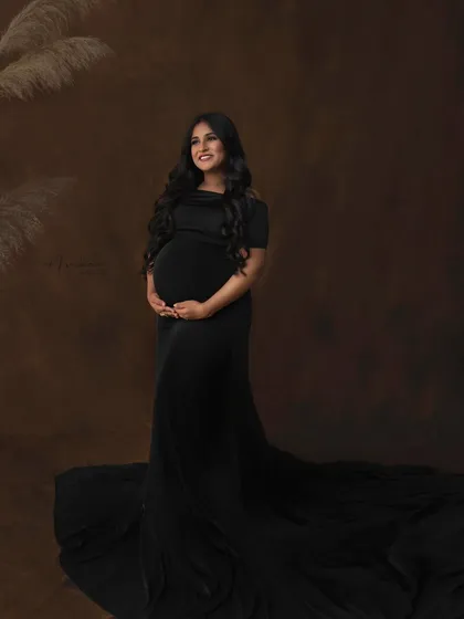 A full-length portrait showing the dramatic sweep of the black gown. The simple, textured backdrop and pampas grass add a touch of warmth and modernity to this classic studio shot.