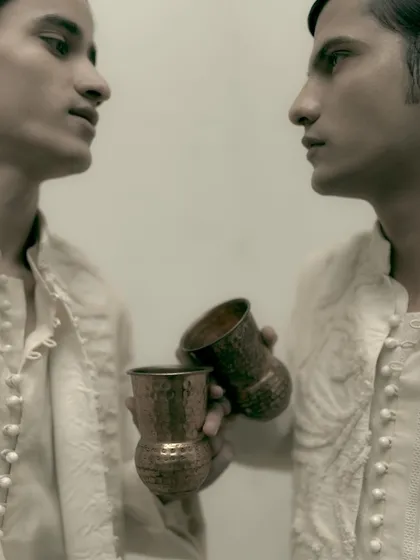 A sepia-toned dual portrait for Sanchit Sharma. The close, mirrored composition creates an intimate and slightly surreal feel, focusing on the models' profiles and the garment details.