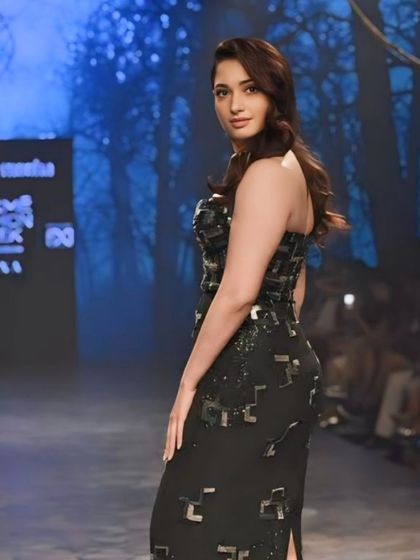 A side view of Tamannaah Bhatia on the runway, set against a moody, forest-like backdrop. This shot highlights the atmosphere of the show.