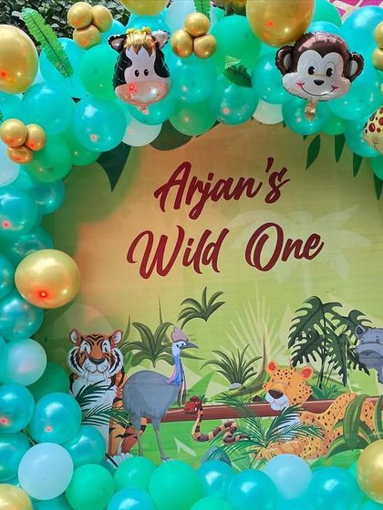 A "Wild One" jungle themed party. The setup features a custom backdrop with jungle animals, framed by a teal and gold balloon arch.