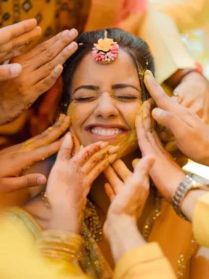 A bride's smile, framed by the loving hands of her family. This is the heart of the Haldi ceremony, a ritual of blessings and happiness.
