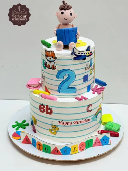 A sweet school-themed cake for a 2nd birthday. This two-tier cake is designed to look like notebook paper, decorated with the alphabet, numbers, and a cute fondant baby reading a book.