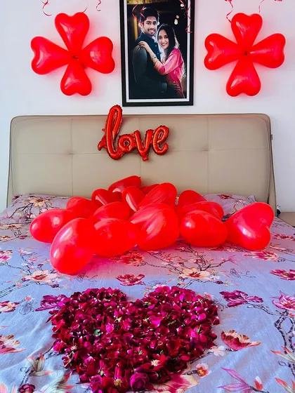 A close-up of the bed decor, featuring a personalized photo frame, a "love" foil balloon, and a heart made from fresh rose petals.