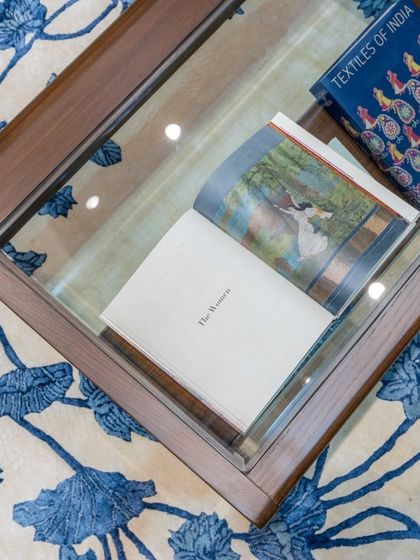 A bespoke coffee table with a glass top, revealing the intricate floral pattern of the rug beneath. This piece was designed to be both functional and a frame for the artistry around it.
