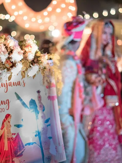 A detail shot of the wedding welcome sign, with the couple blurred in the background as they walk to the mandap.