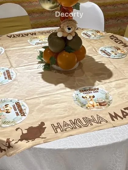 A close-up of the guest table decor. Each table features a custom Lion King themed tablecloth and a balloon centerpiece with a small lion plushie.