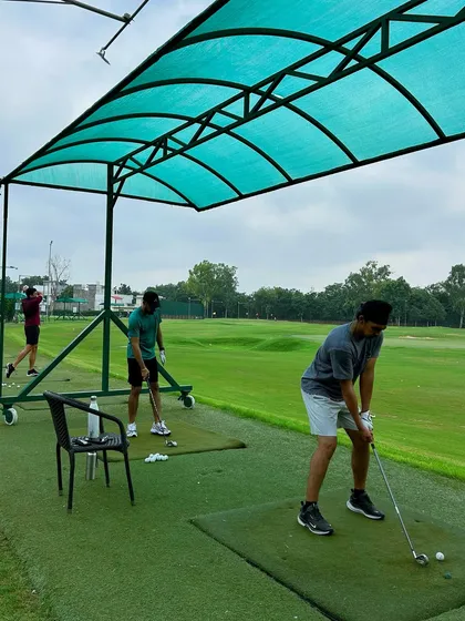 Three golfers practicing in a row under a covered bay, each focused on their own technique.